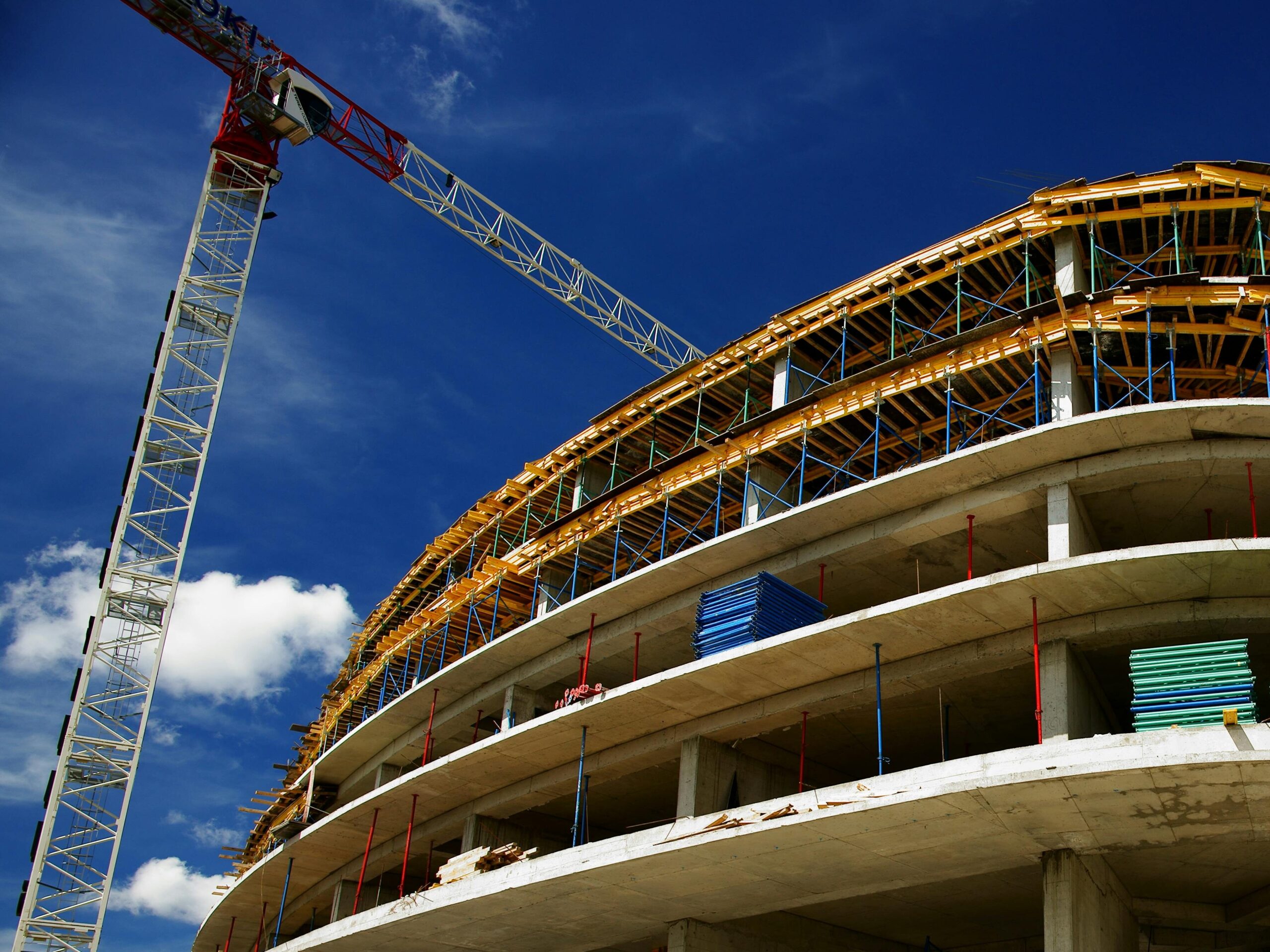 Low angle view of a circular building under construction with a crane, clear blue sky.